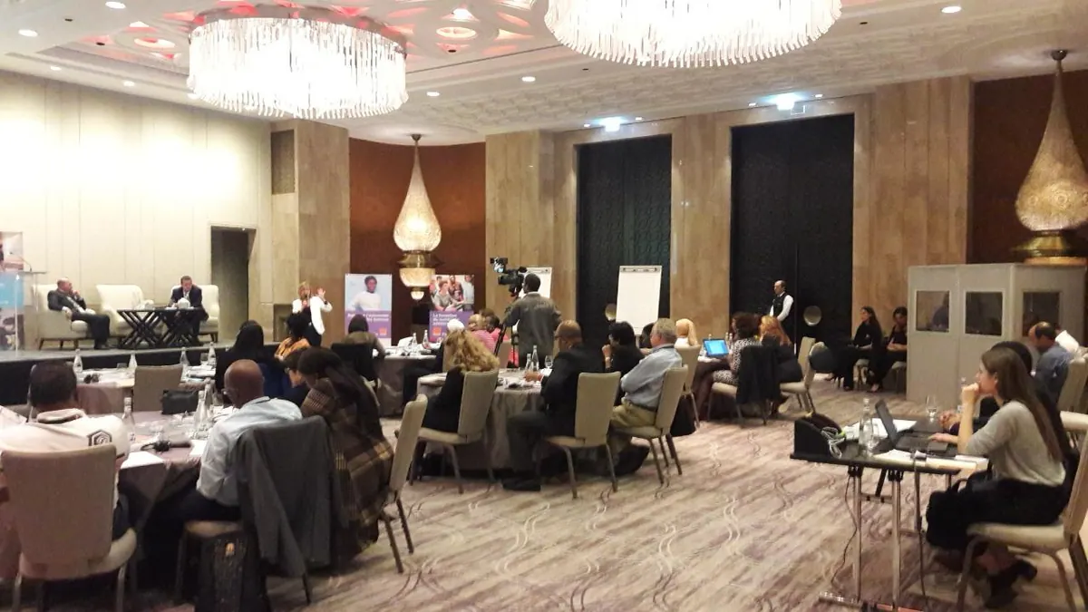 Interprétation de conférence lors d’un événement professionnel : participants autour de tables rondes et cabine d’interprétation au fond de la salle