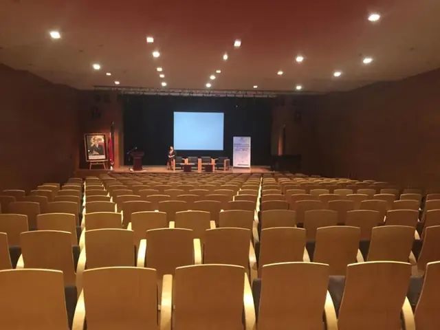 Auditorium avec rangées de fauteuils et écran de projection, préparé pour une conférence