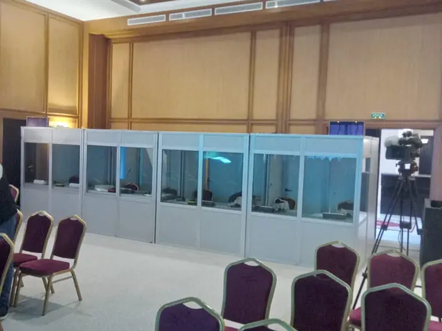 Quatre cabines d’interprétation simultanée installées au fond d’une salle de conférence, à côté d’une caméra