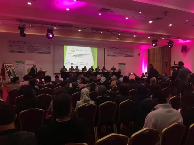 Conférence professionnelle devant un large public, intervenants à la tribune dans une salle éclairée en rose