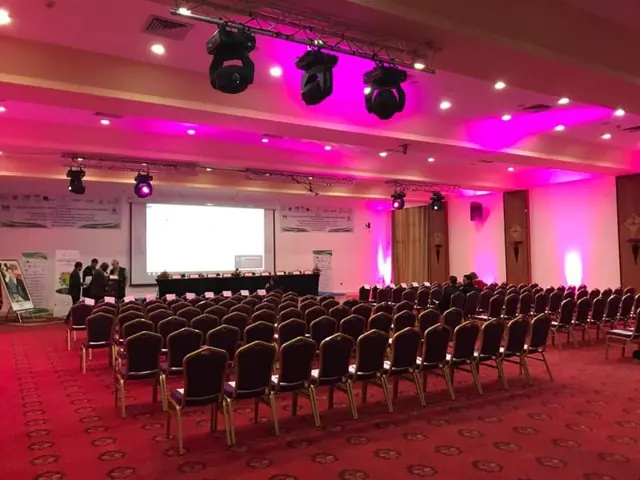 Salle de conférence aux éclairages roses, rangées de chaises et tribune avant le début d’un événement